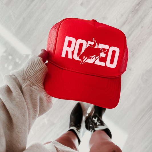 Red and white rodeo trucker hat with bold western graphic styled on denim with sunglasses