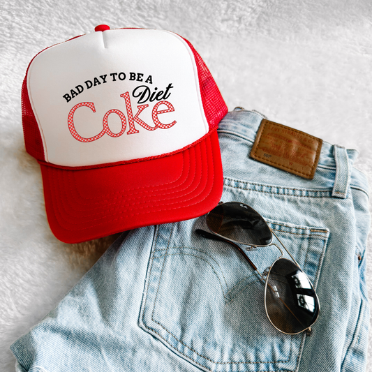 Red and white foam trucker hat with “Bad Day to Be a Diet Coke” retro graphic styled with denim and sunglasses
