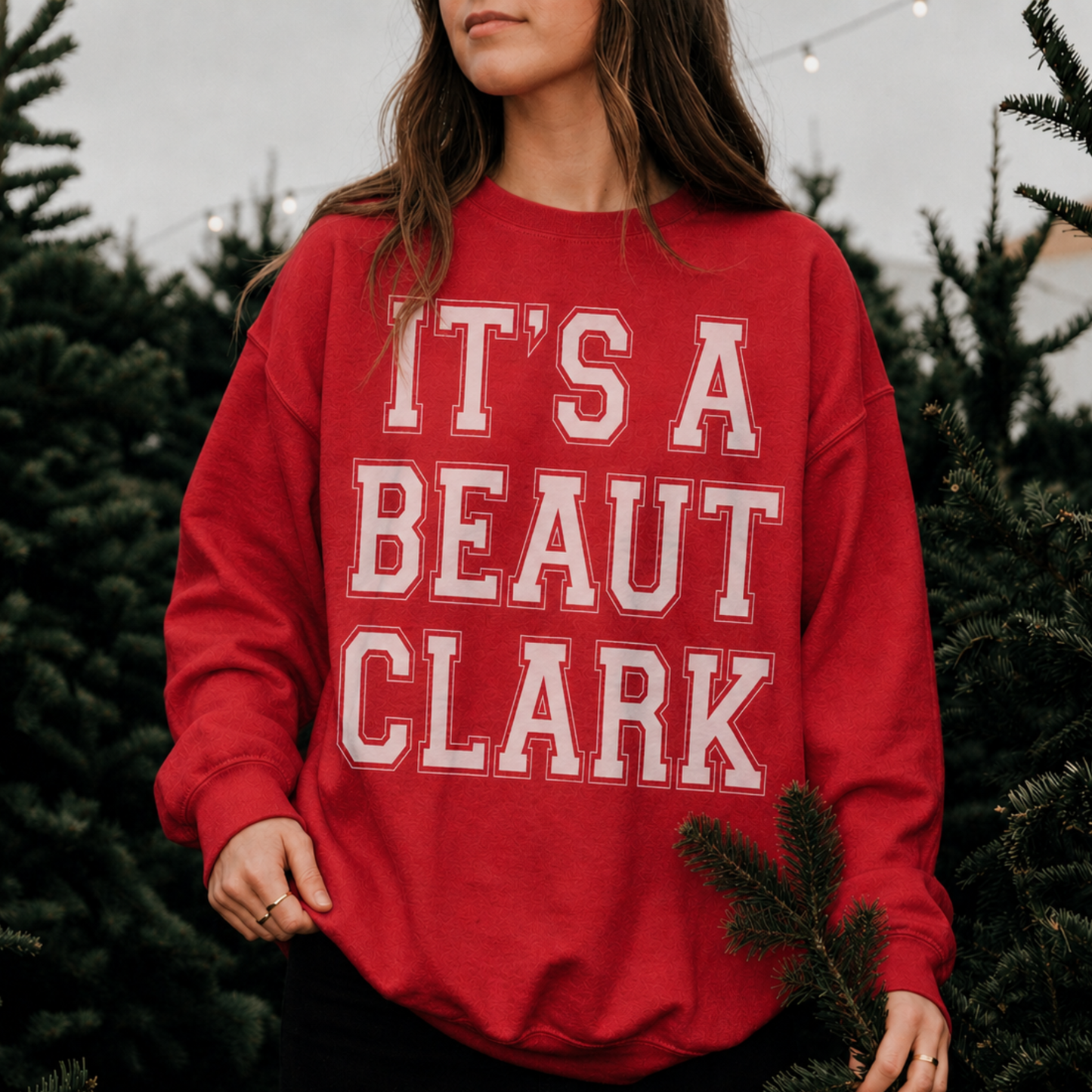 Woman wearing red It's a Beaut Clark Christmas sweatshirt with white graphic at a festive Christmas tree farm.