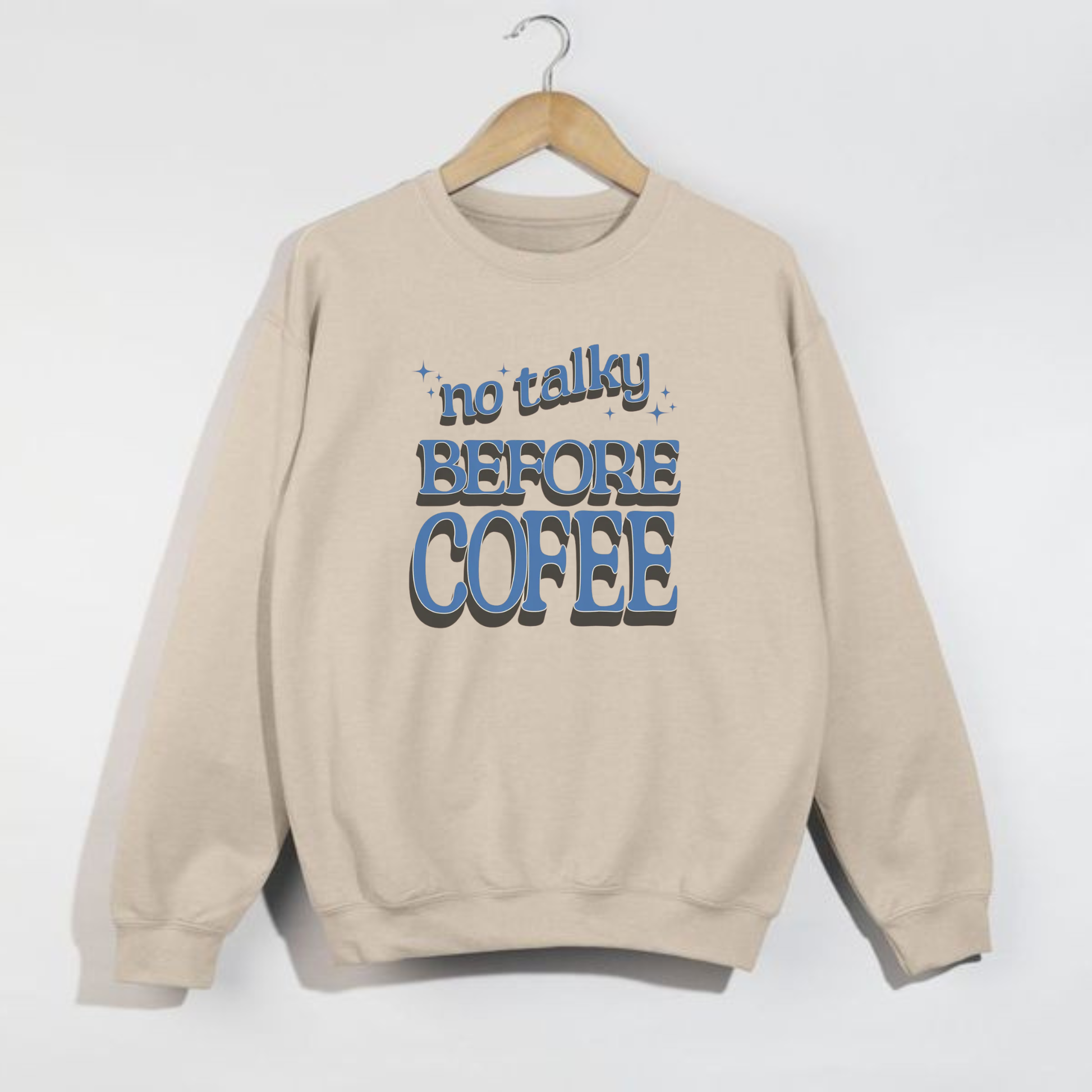 Sand crewneck sweatshirt with blue retro ‘No Talky Before Coffee’ design hanging on wooden hanger