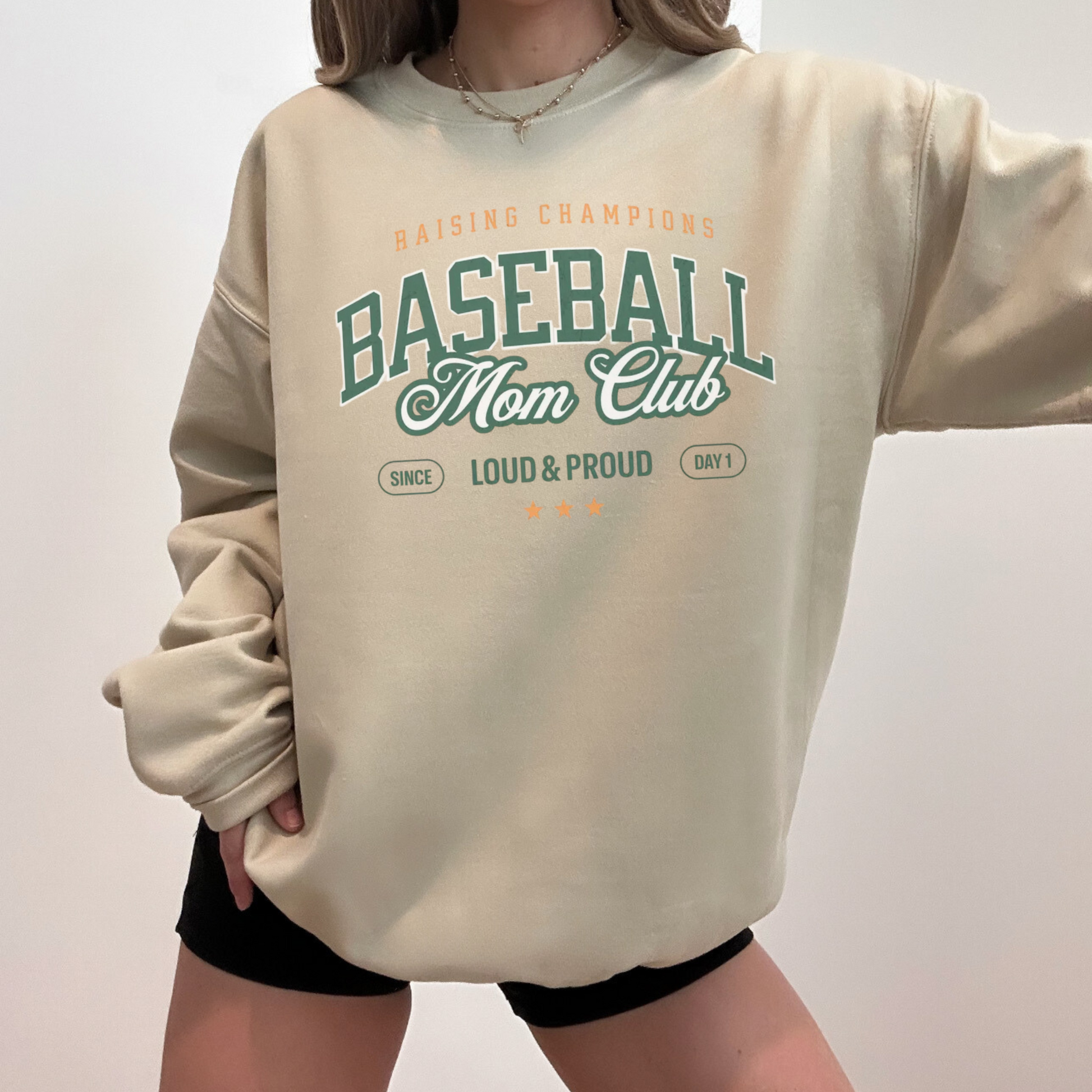 Model wearing a sand “Baseball Mom Club” crewneck sweatshirt with black shorts.