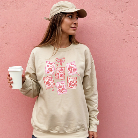 Woman wearing sand-colored Valentine stamps sweatshirt with soft pink romantic graphics.