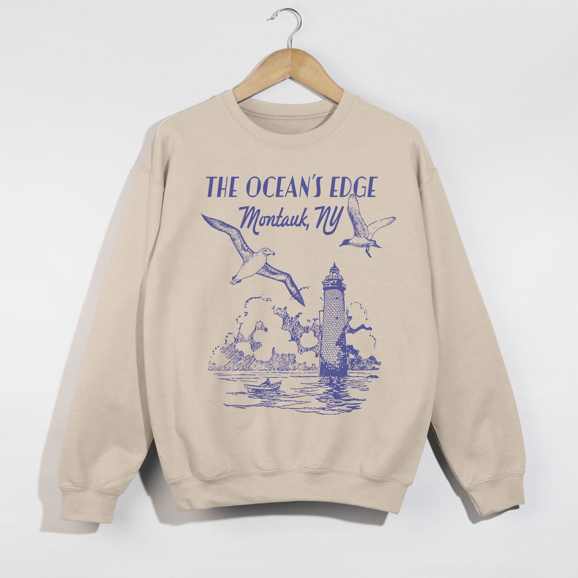 "Sand-colored Montauk coastal lighthouse graphic sweatshirt hanging on wooden hanger."
