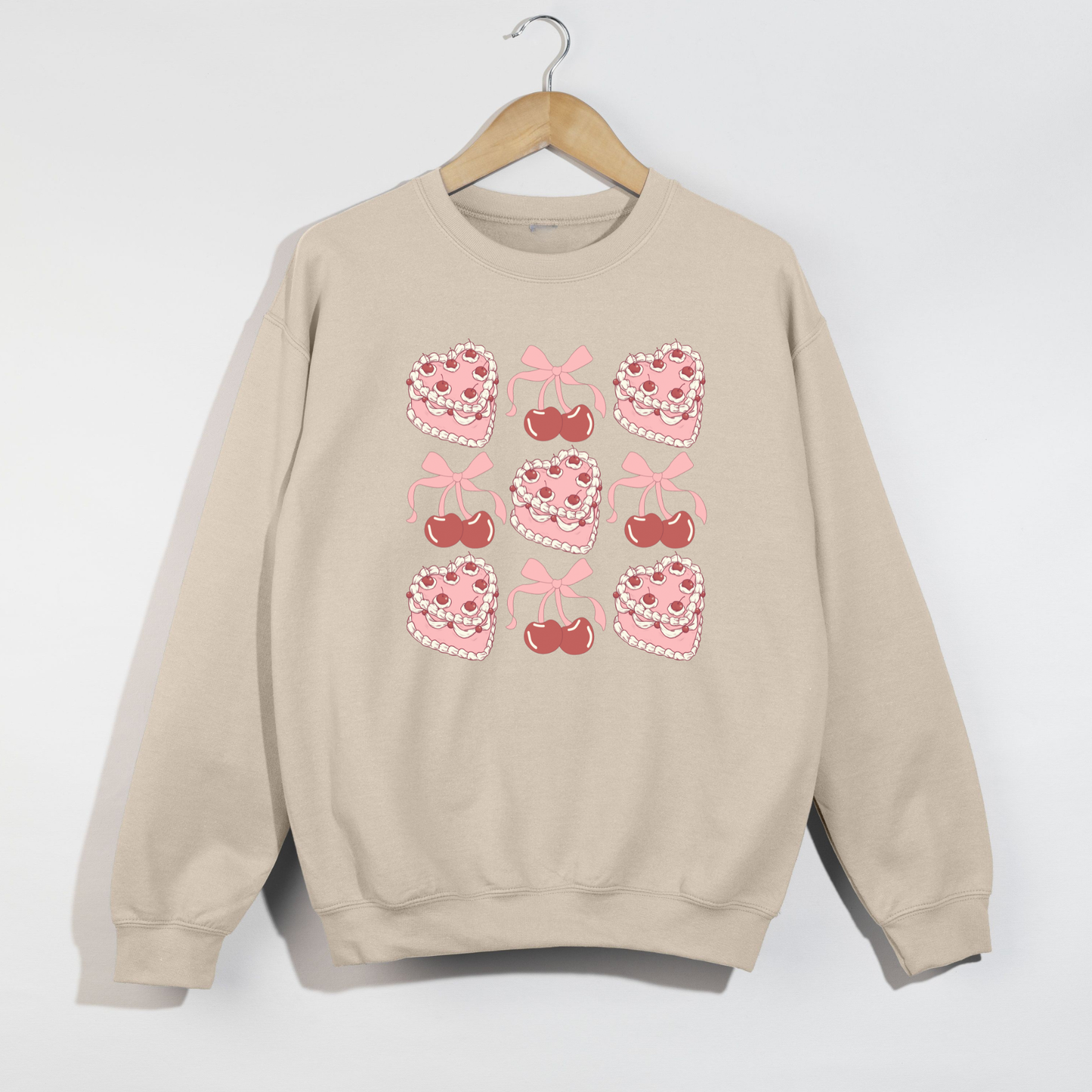 Sand-colored Valentine crewneck on hanger displaying pink vintage-inspired heart cake and cherry graphics in a grid layout.