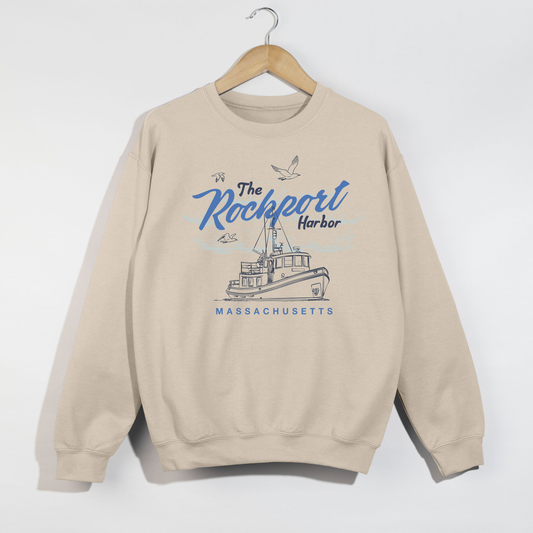 Beige sweatshirt with 'The Rockport Harbor, Massachusetts' design on a hanger against a white background