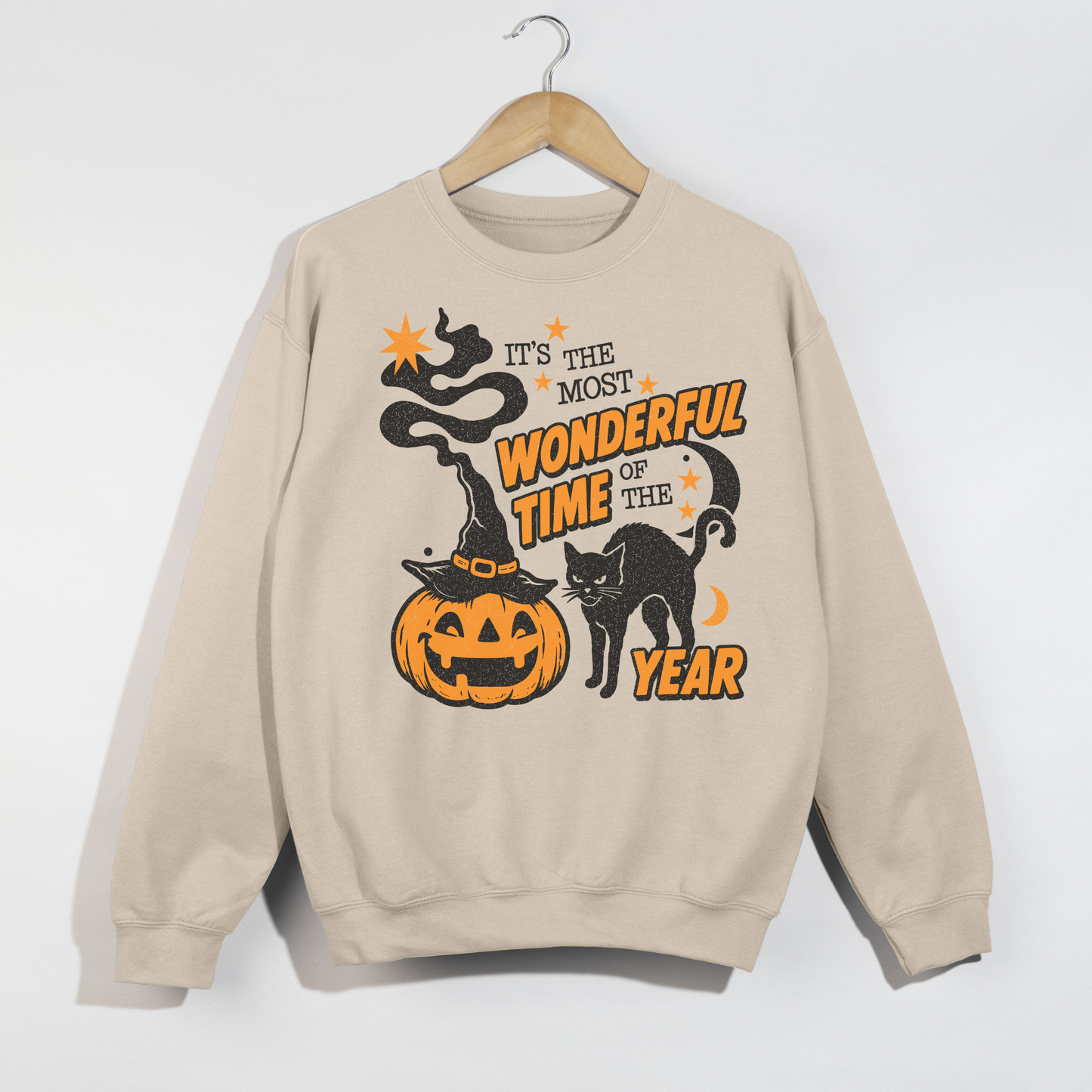 Sand Halloween sweatshirt featuring a distressed pumpkin wearing a witch hat with black cat and "It's the Most Wonderful Time of the Year" graphic hanging on a wooden hanger.