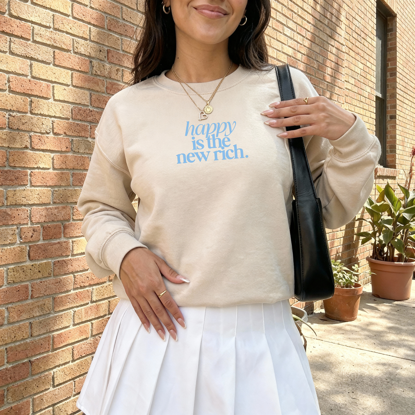 Beige crewneck sweatshirt featuring “happy is the new rich.” minimalist graphic styled outdoors