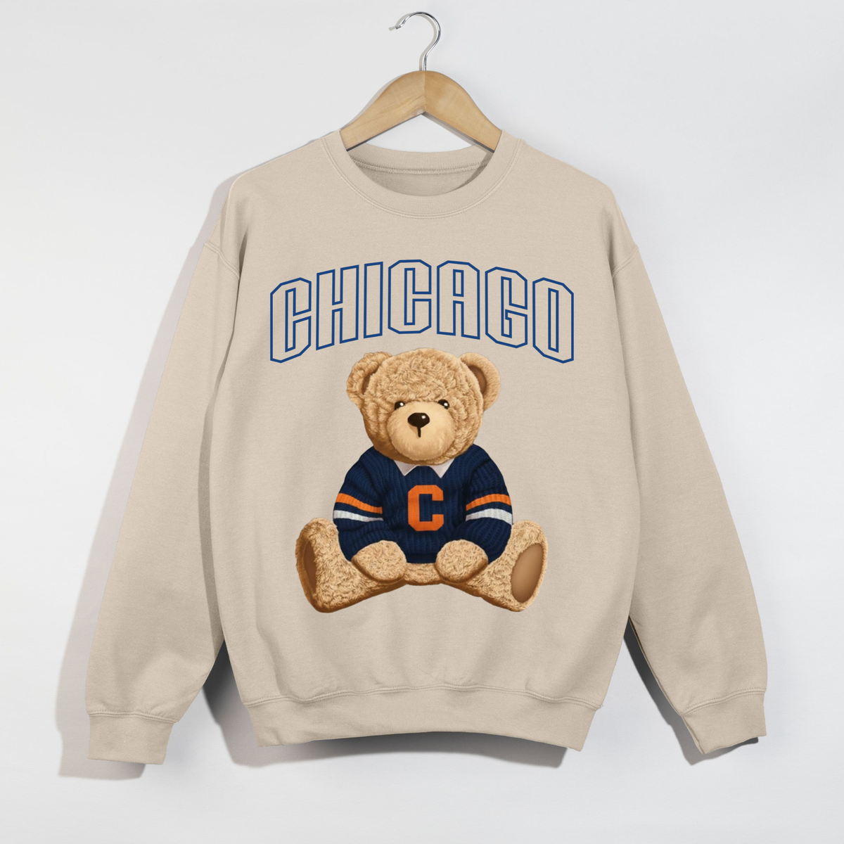 Sand Chicago teddy bear sweatshirt displayed on wooden hanger featuring navy outlined varsity letters and football teddy bear