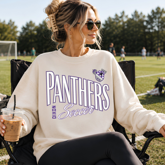 Woman wearing sand Dixon Panthers Soccer crewneck sweatshirt at a soccer field with purple and white Panthers graphic
