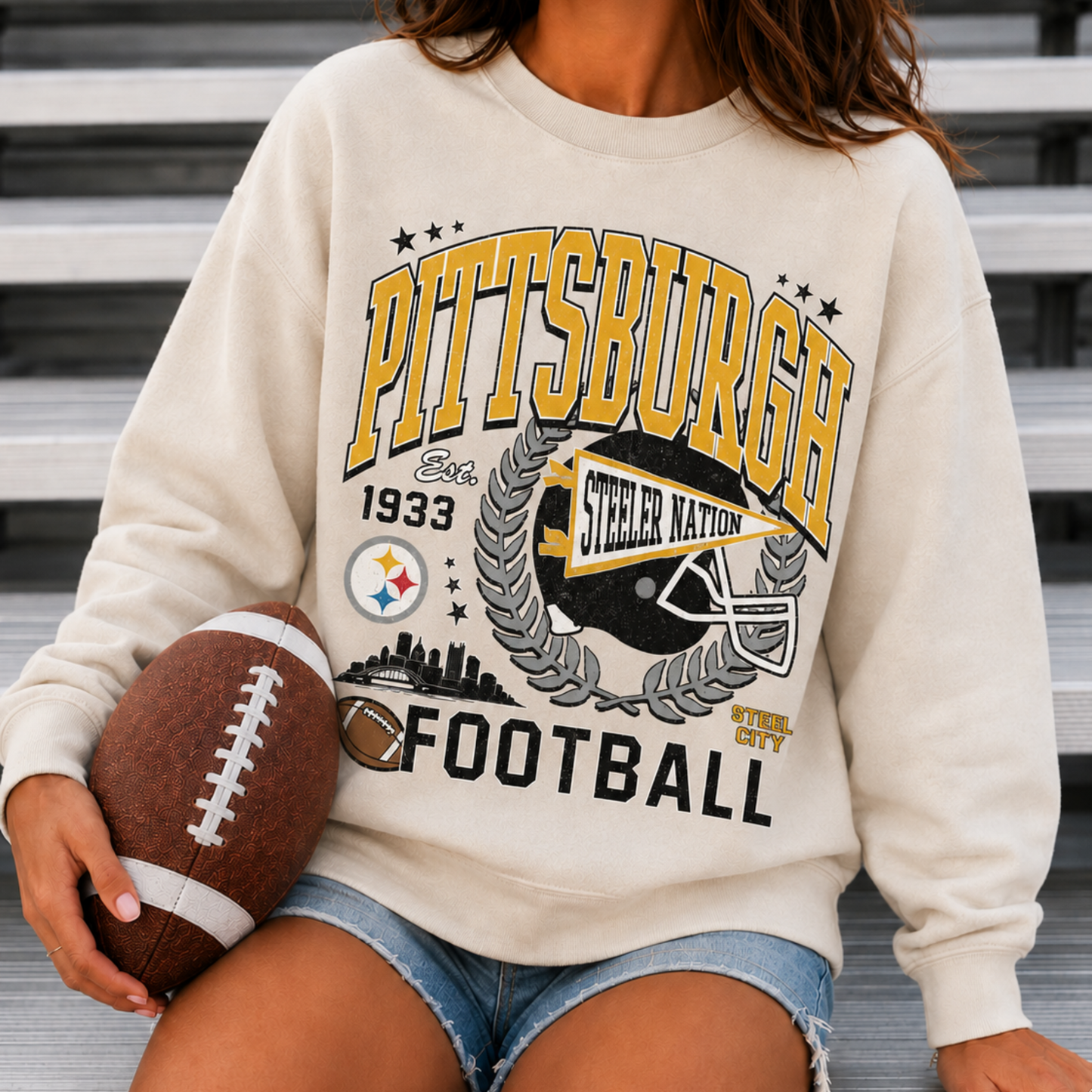 Woman wearing cream Pittsburgh football sweatshirt with black and gold Steel City graphic at football stadium