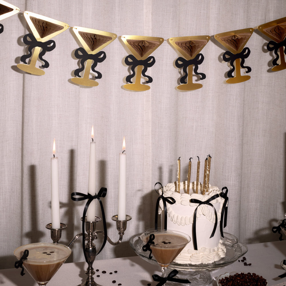 Decorative setup with cake, candles, and martini-themed decor against a light gray curtain.