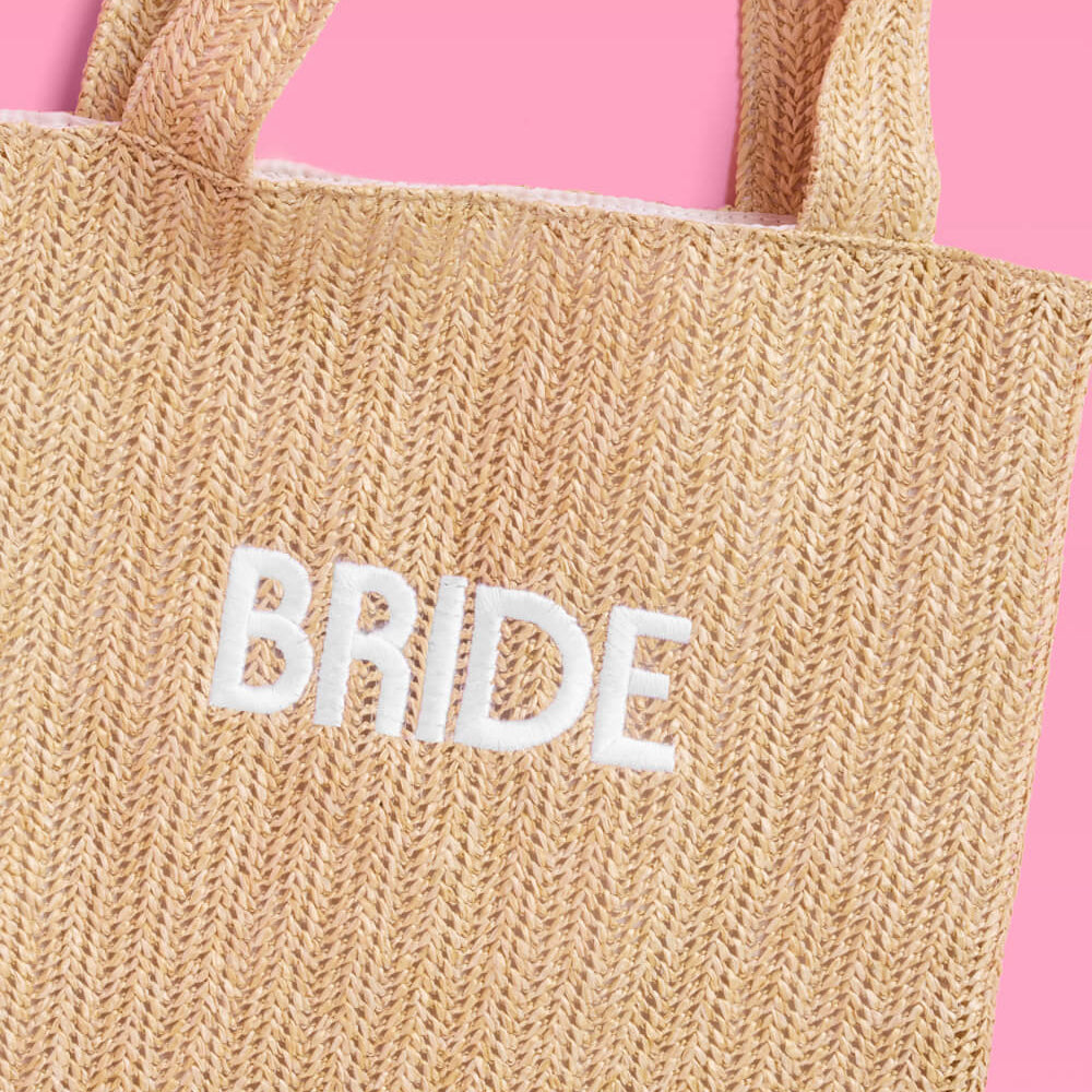 Beige tote bag with 'BRIDE' embroidery on a pink background