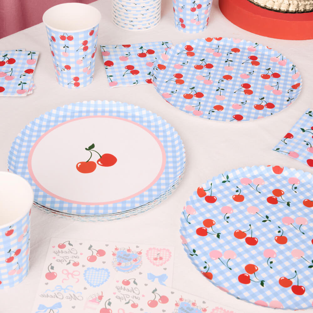 Table setting with cherry-themed paper plates, cups, and napkins on a white table.