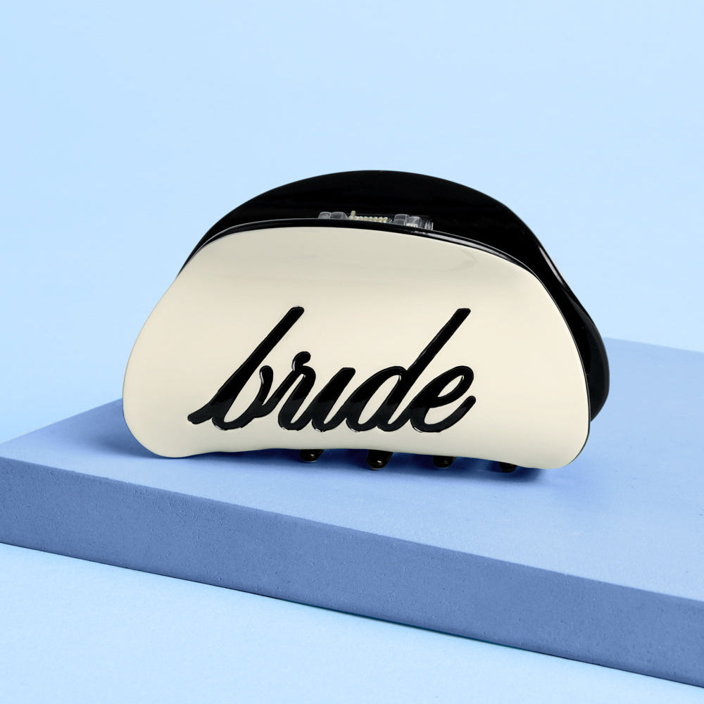 Ivory bride claw clip with black recessed logo on blue background close-up detail
