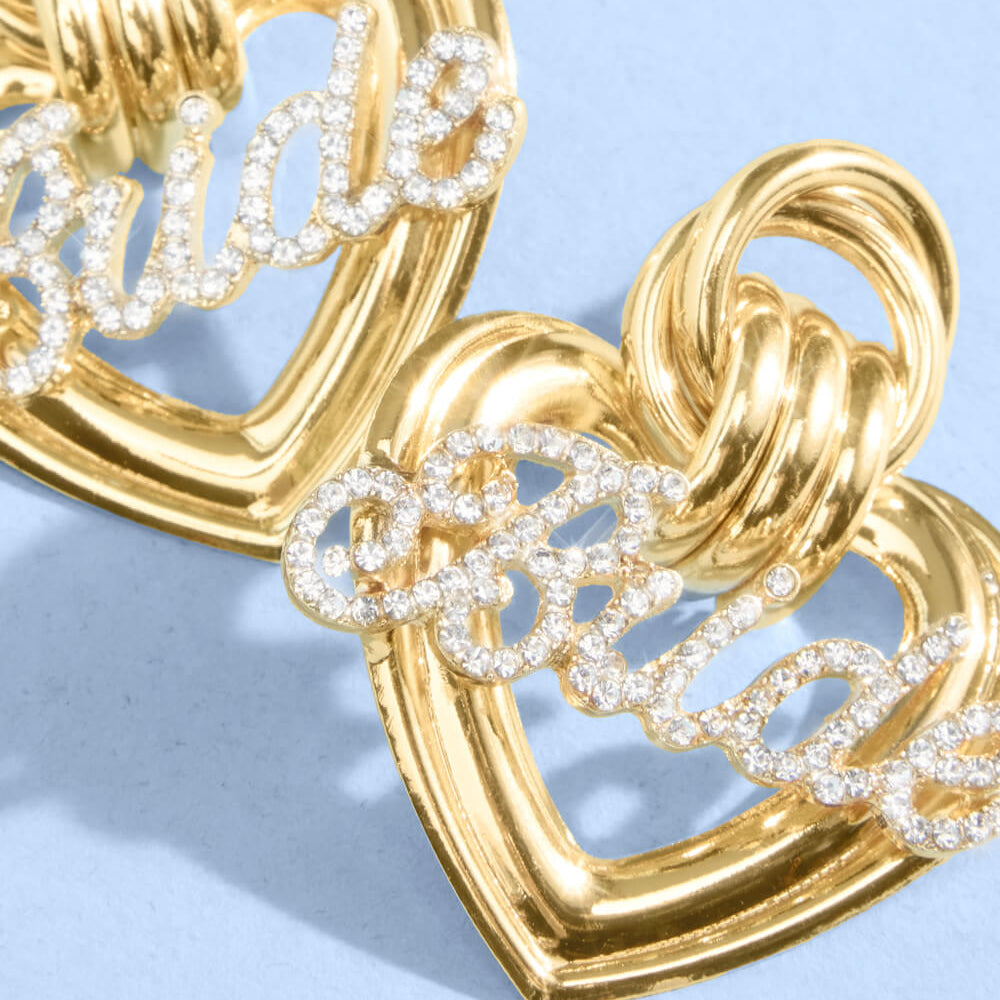 Close up of gold metal heart bridal earrings with crystal rhinestone script