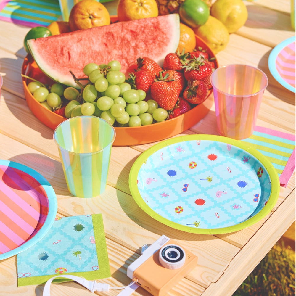 Colorful outdoor setting with fruit platter, plates, and cups on a wooden table.