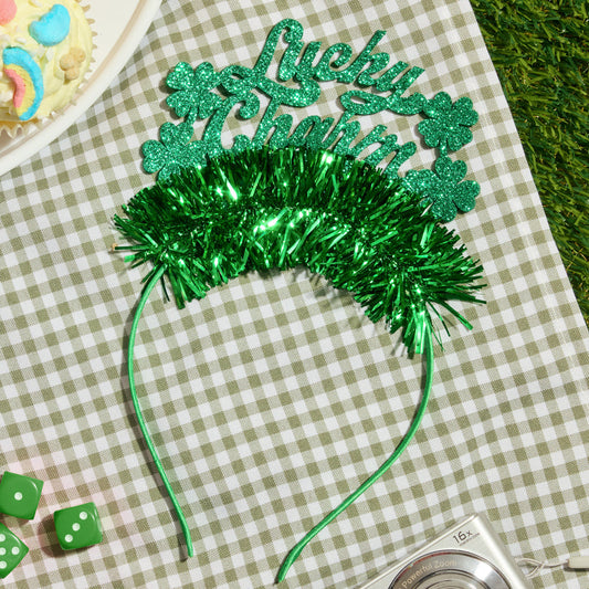 Green festive headband with 'Lucky' text on a checkered tablecloth with cupcakes and dice.