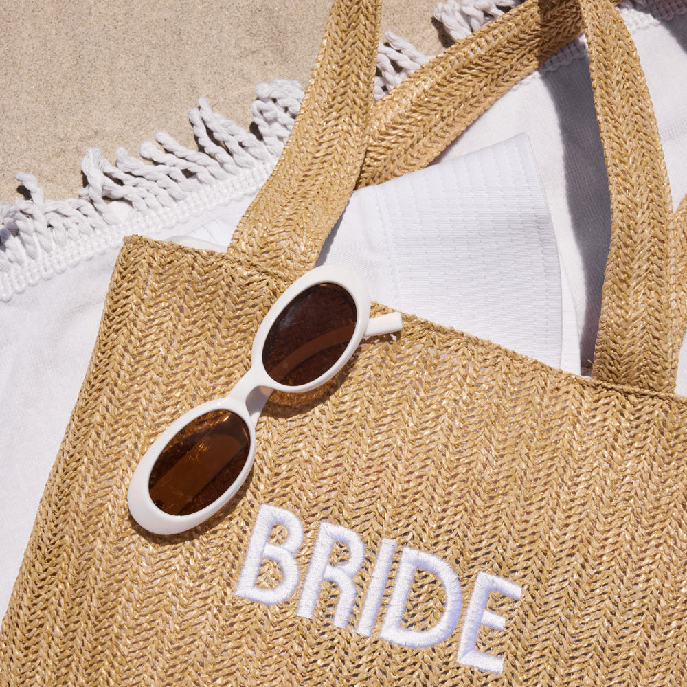 Beige tote bag with 'BRIDE' embroidery and sunglasses on a white background