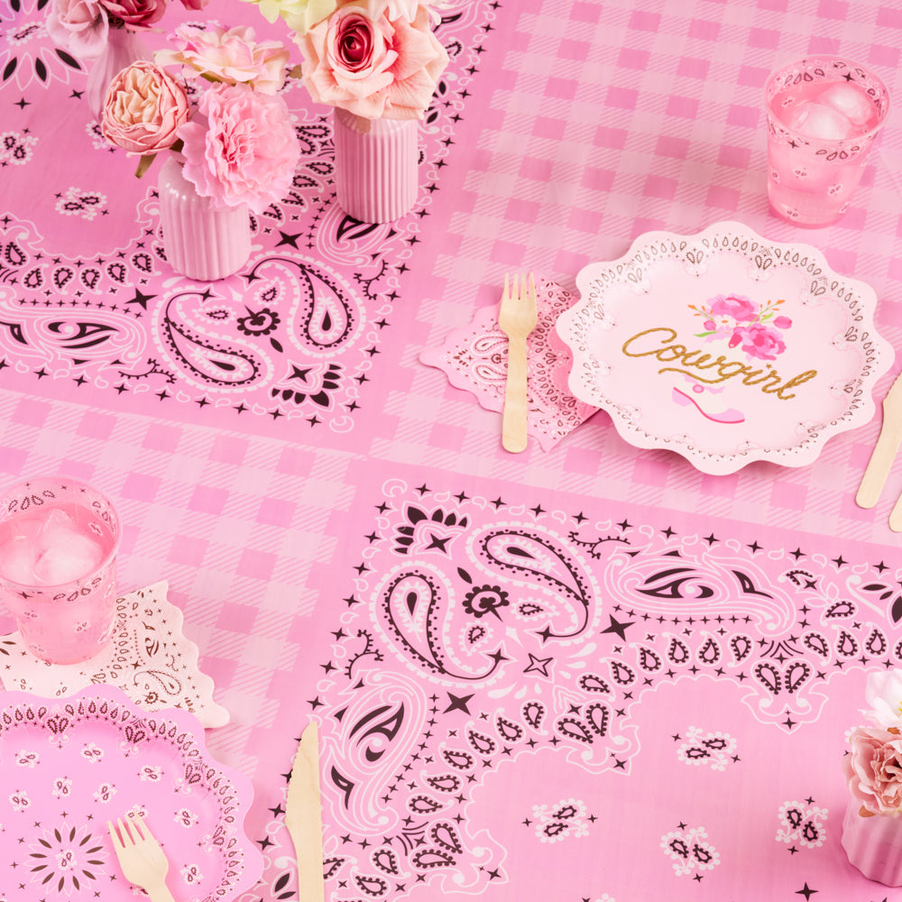 Pink tablecloth with cowboy-themed decorations including bandanas, plates, and cutlery.