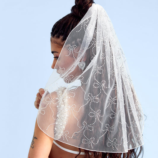 Woman wearing a white veil with bow patterns against a clear blue sky.
