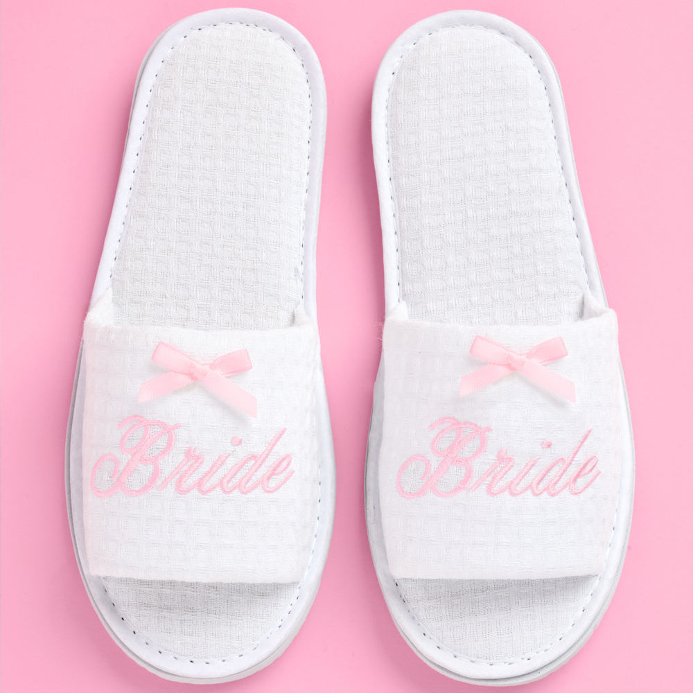 White slippers with 'Bride' text and pink bows on a pink background