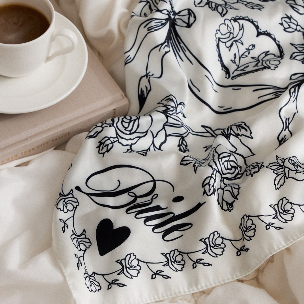 White fabric with black floral and heart designs, including the word 'Pride', on a soft white background.