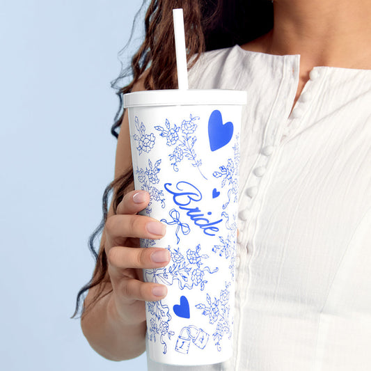 Person holding a white tumbler with blue floral and heart designs, and the word 'Bride' on a light blue background.