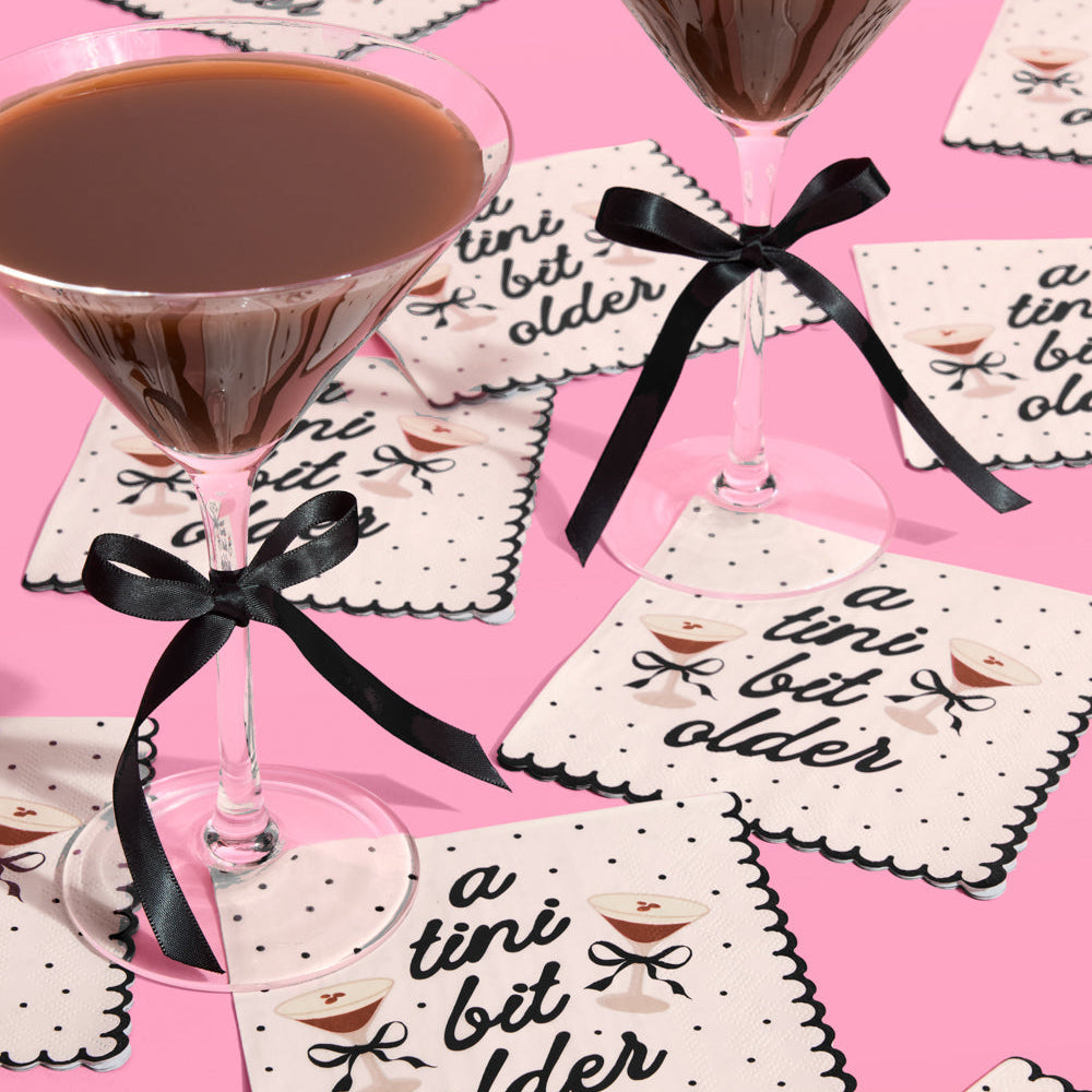 Two martini glasses with chocolate cocktails on a pink background with decorative espresso martini printed napkins.