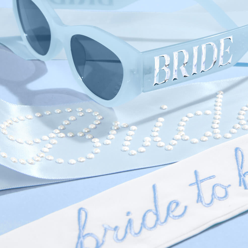 Sunglasses and sash with 'BRIDE' and 'bride to be' text on a light blue background