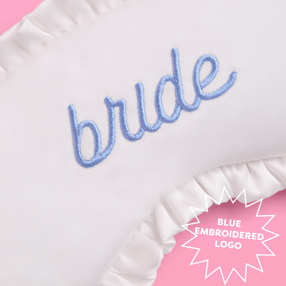 White sleep mask with blue 'bride' embroidery on a pink background
