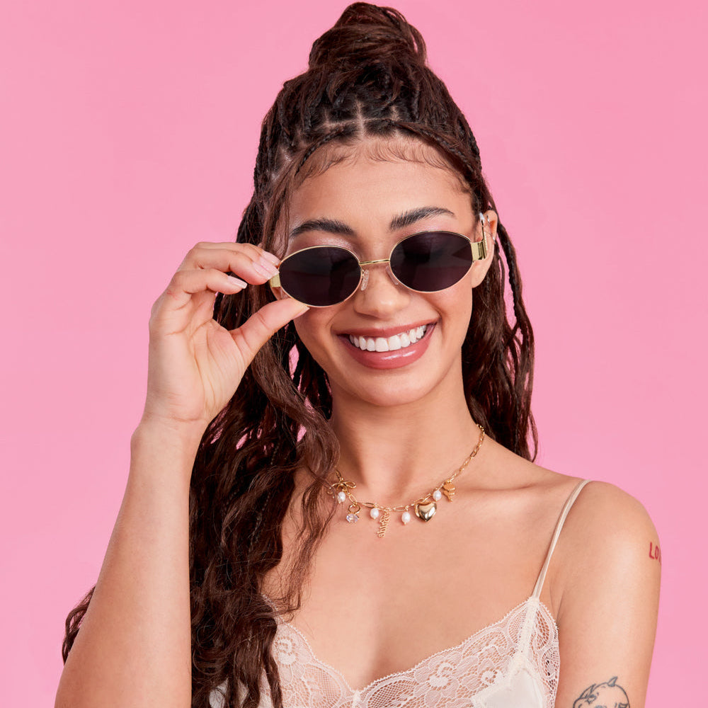 Woman wearing sunglasses and a white lace top against a pink background