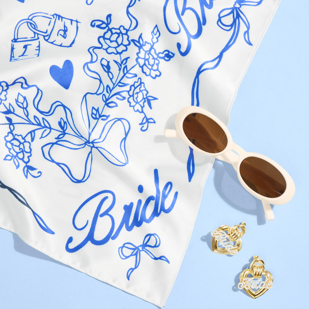 White scarf with blue 'Bride' text and floral patterns, sunglasses, and earrings on a light blue background