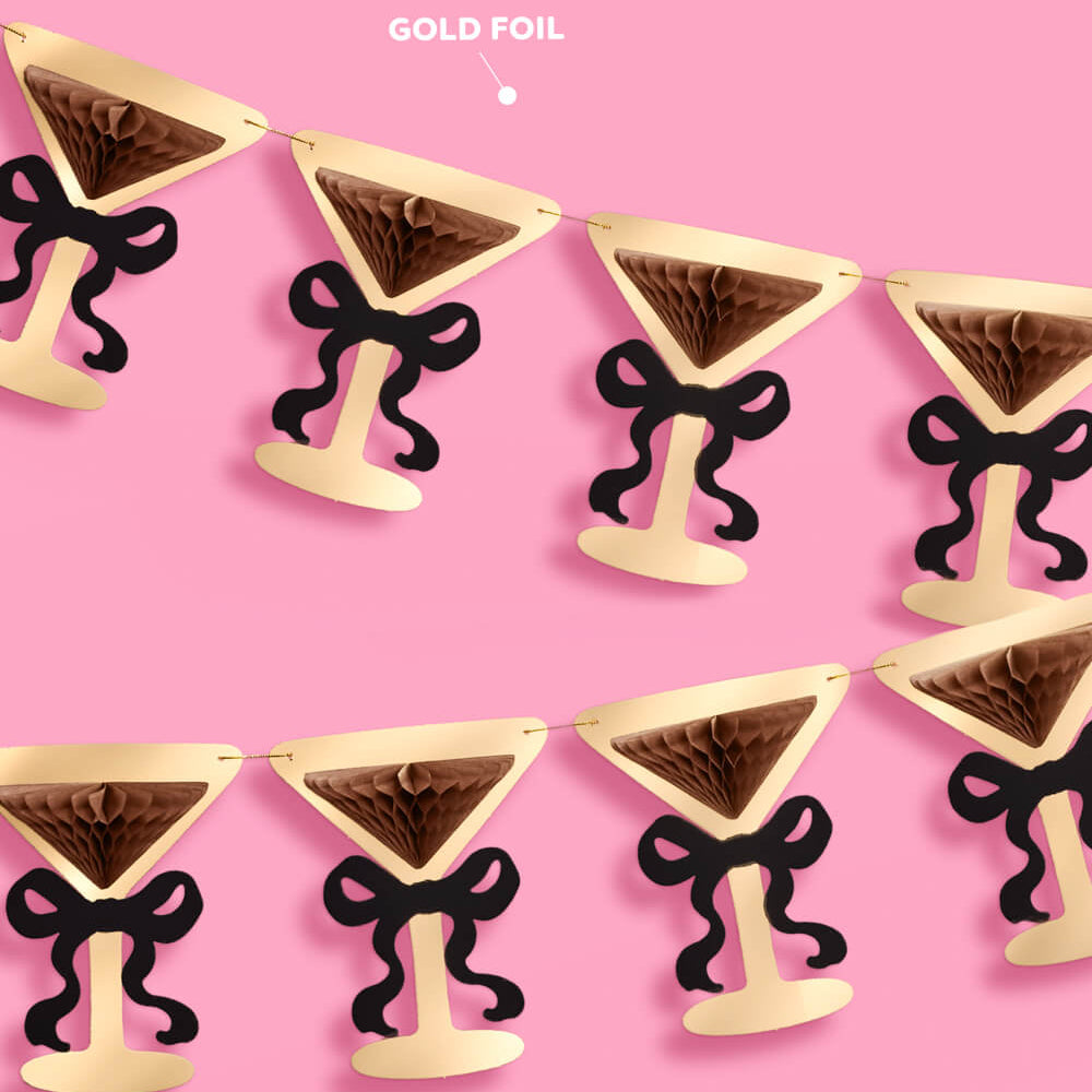 Gold foil cocktail glass-shaped decorations with black bows on a pink background