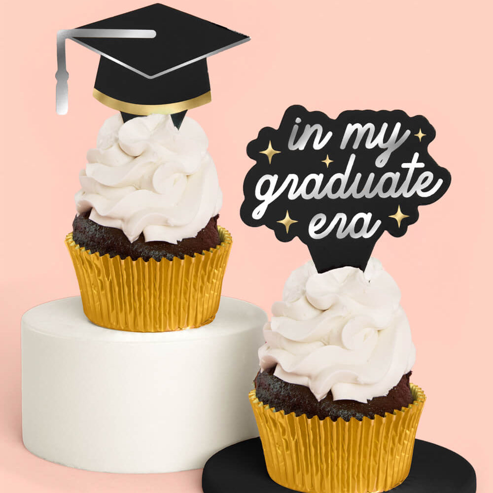 Two cupcakes with graduation-themed toppers on a pink background