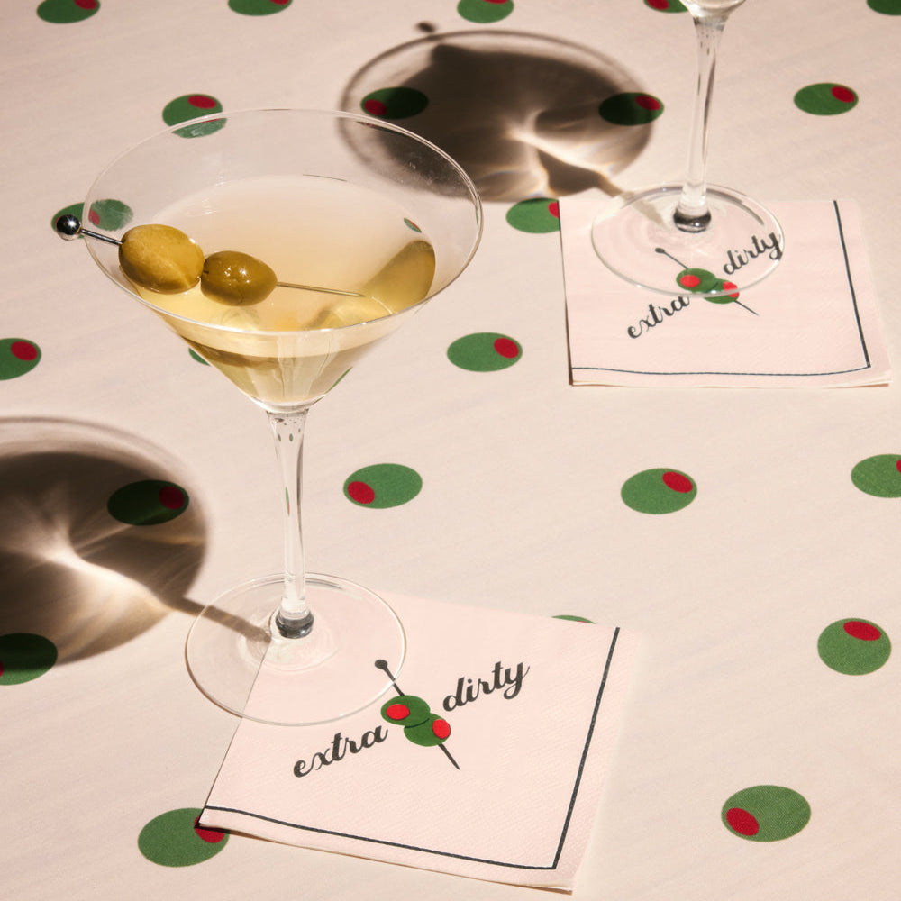 Two martini glasses with olive garnishes on a polka dot tablecloth with 'extra dirty' napkins.