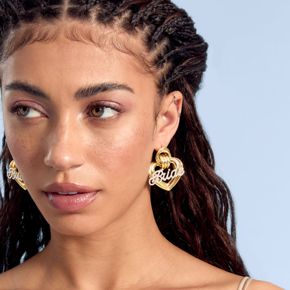Model wearing gold heart bride statement earrings with rhinestone lettering
