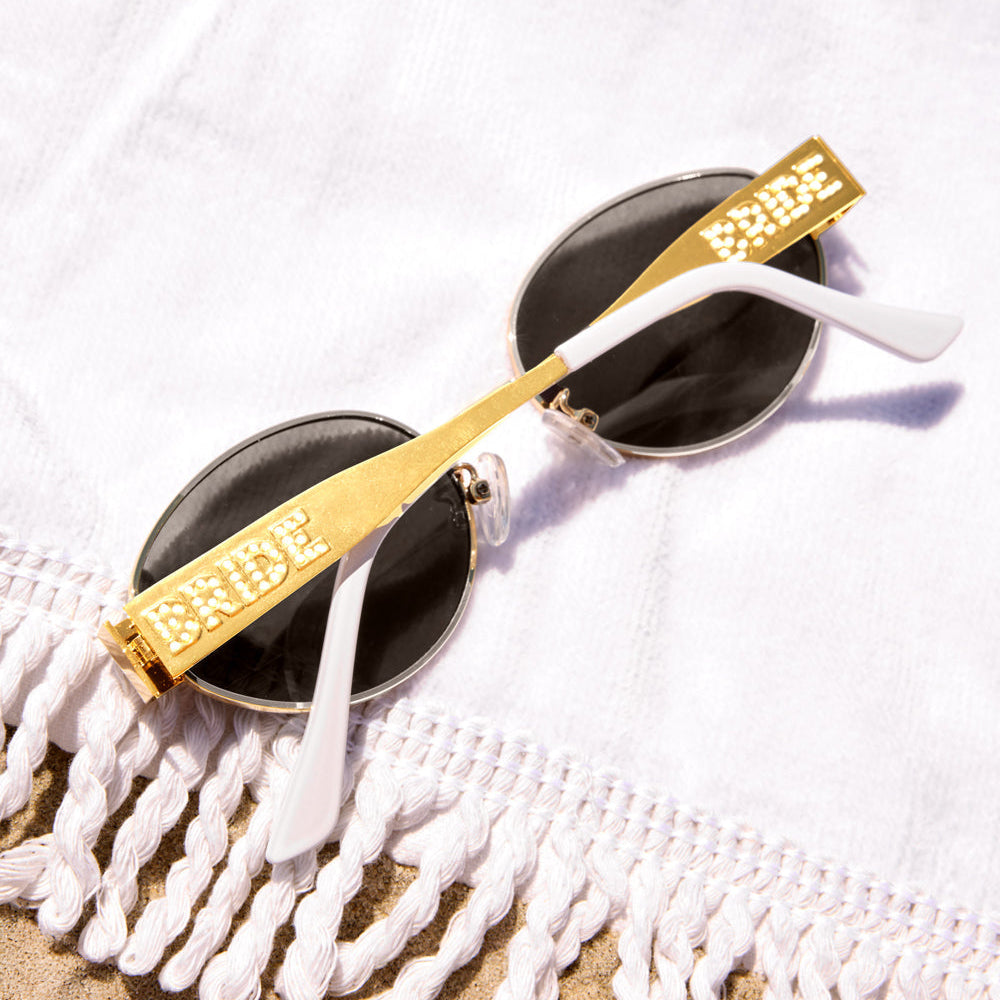 Sunglasses with gold frame and 'Bride' text on a white textured surface