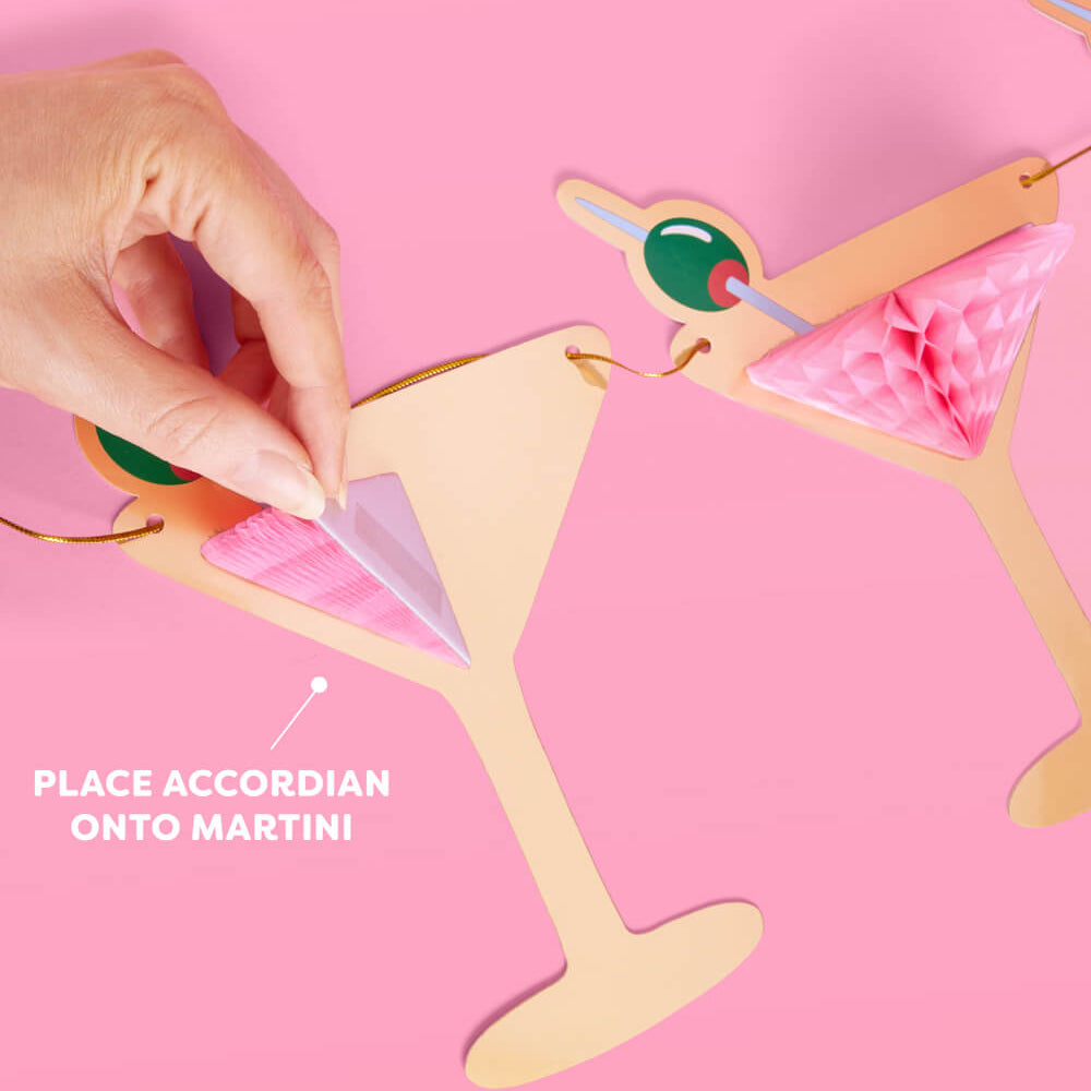 Hand placing an accordian onto a martini-shaped card with pink background