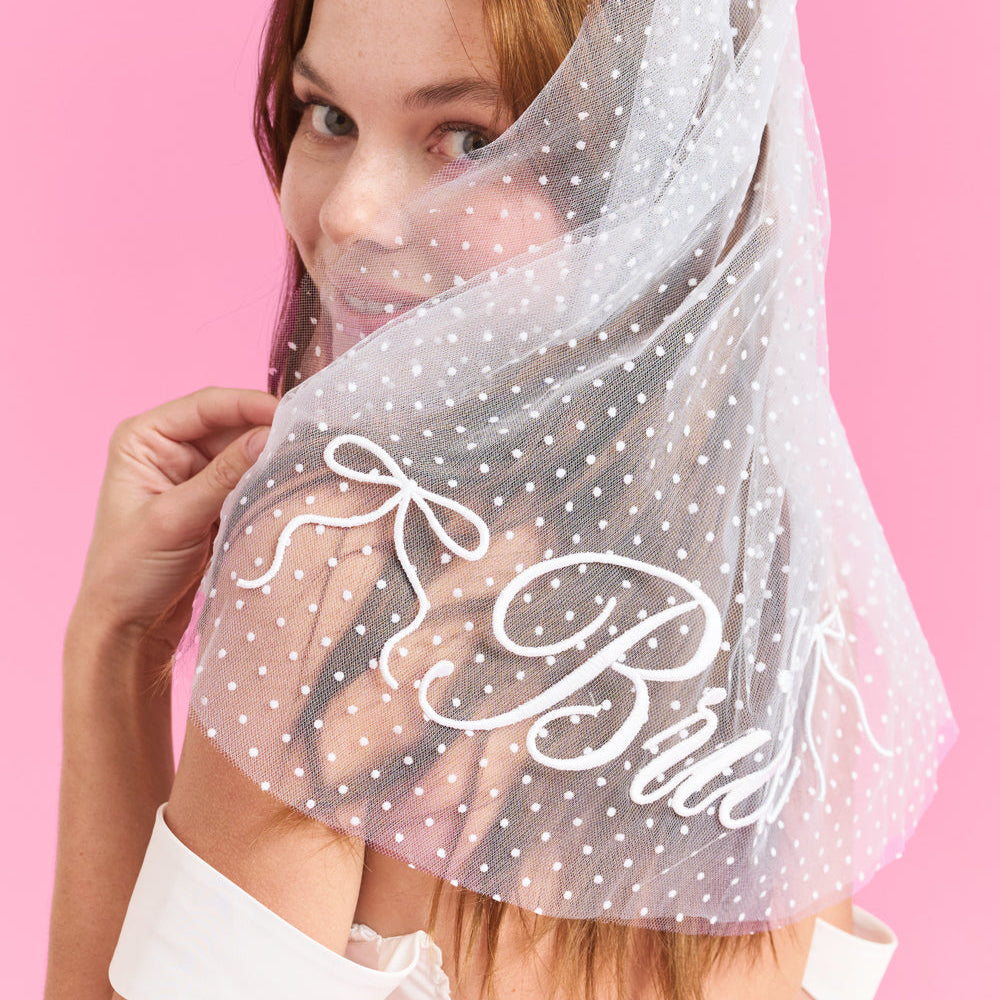 Woman wearing a polka dot veil with 'Bride' text on a pink background