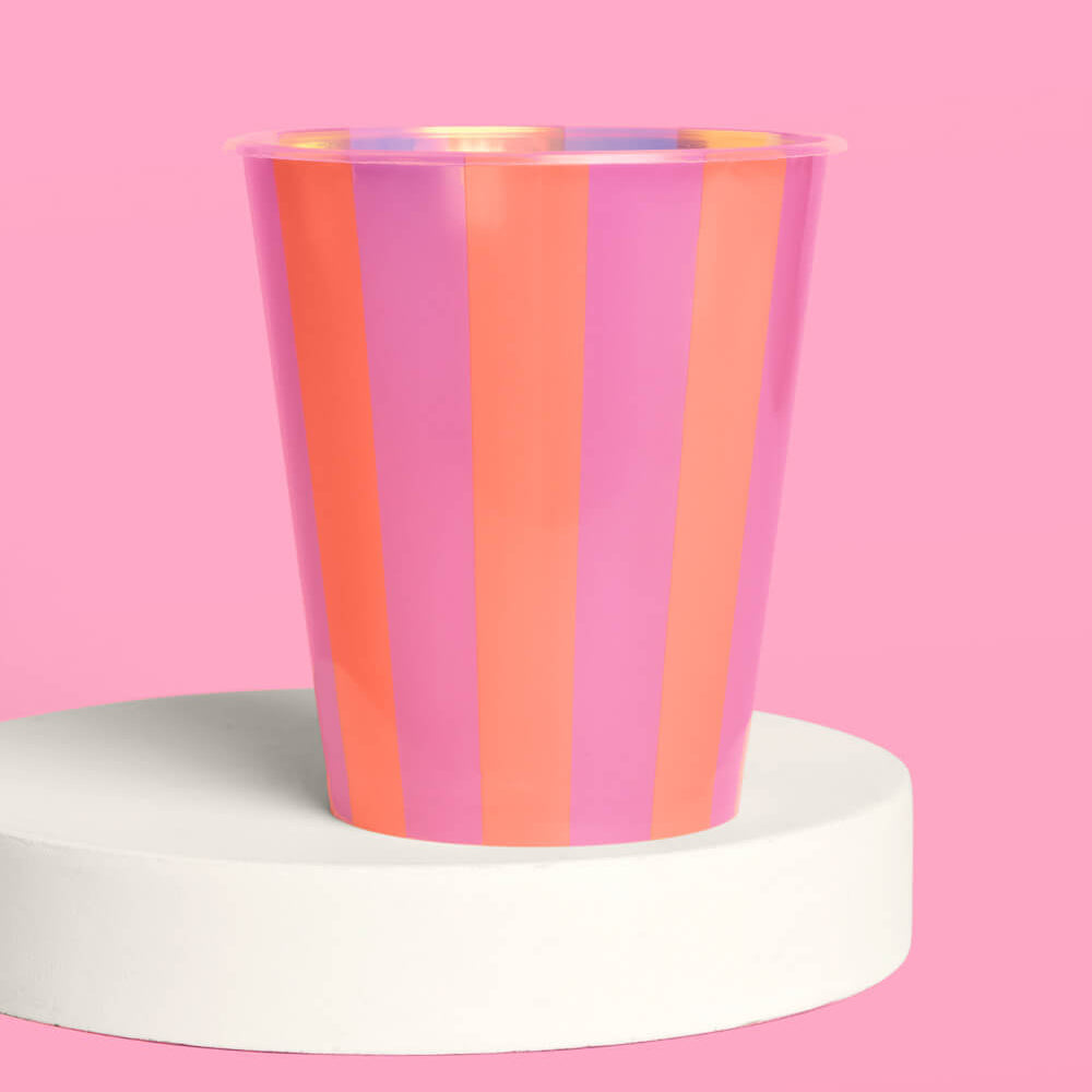 Colorful striped cup on a white pedestal against a pink background