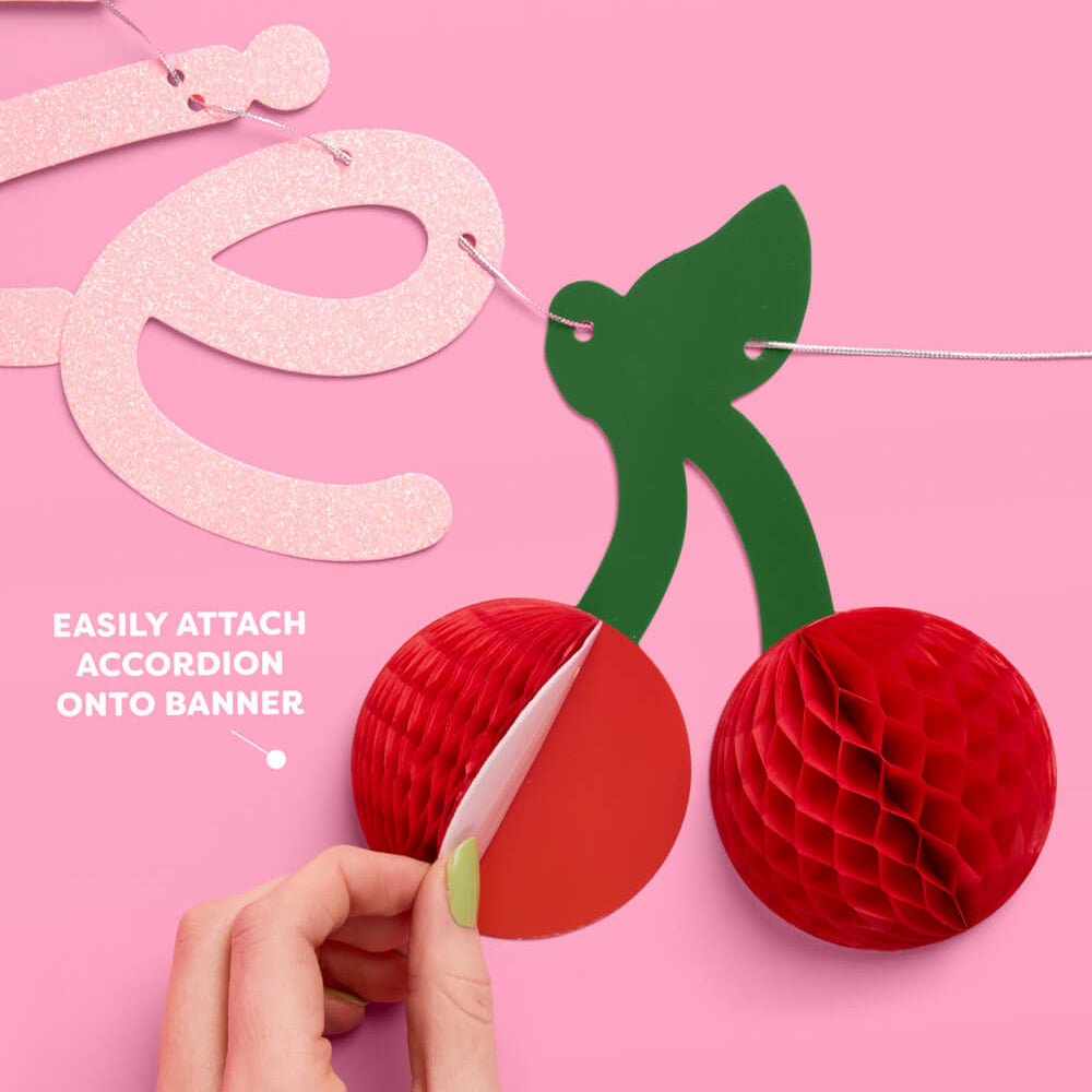 Decorative paper garland with red honeycomb balls and green leaves on a pink background.