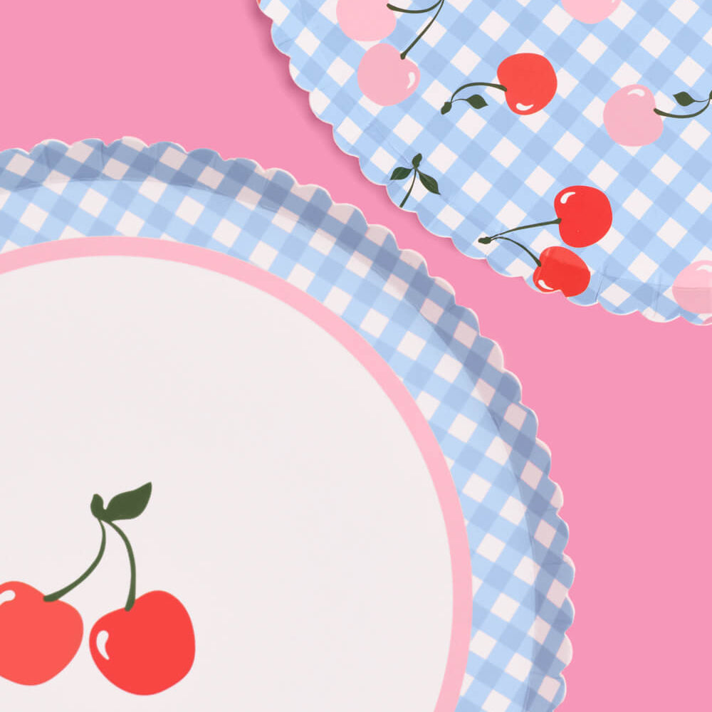 Two paper plates with blue gingham pattern and red cherries on a pink background