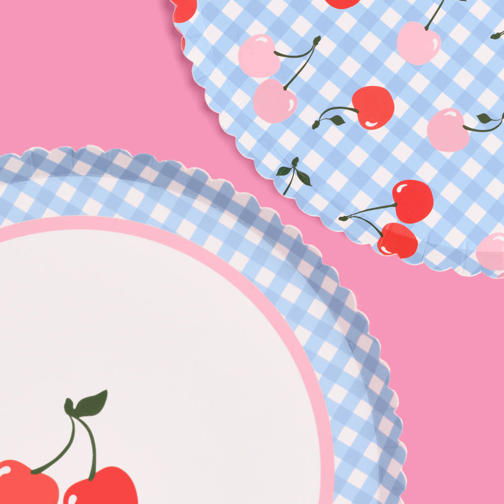 Two paper plates with blue gingham pattern and red cherries on a pink background