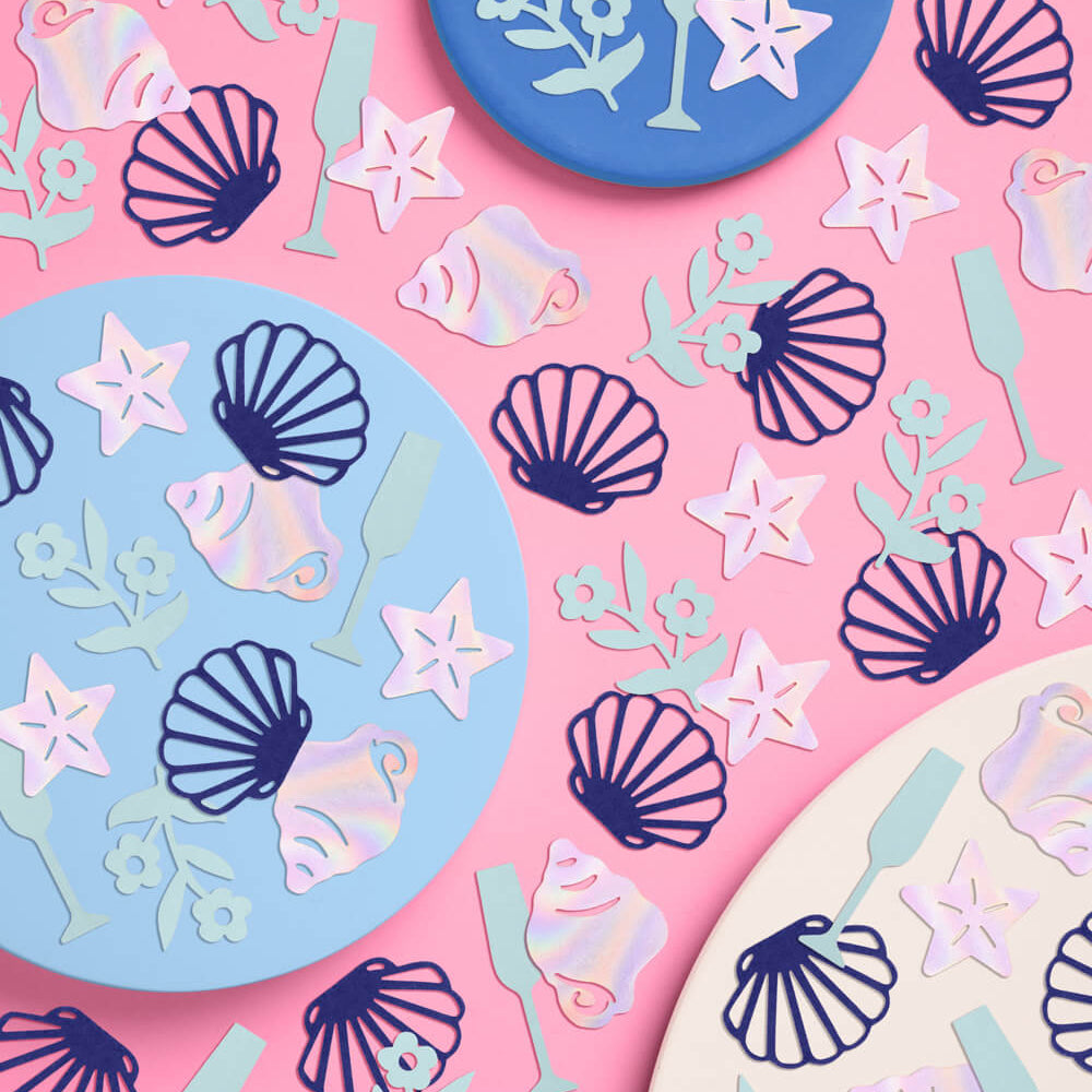 Decorative paper plates with shell, starfish, and fish patterns on a pink background.
