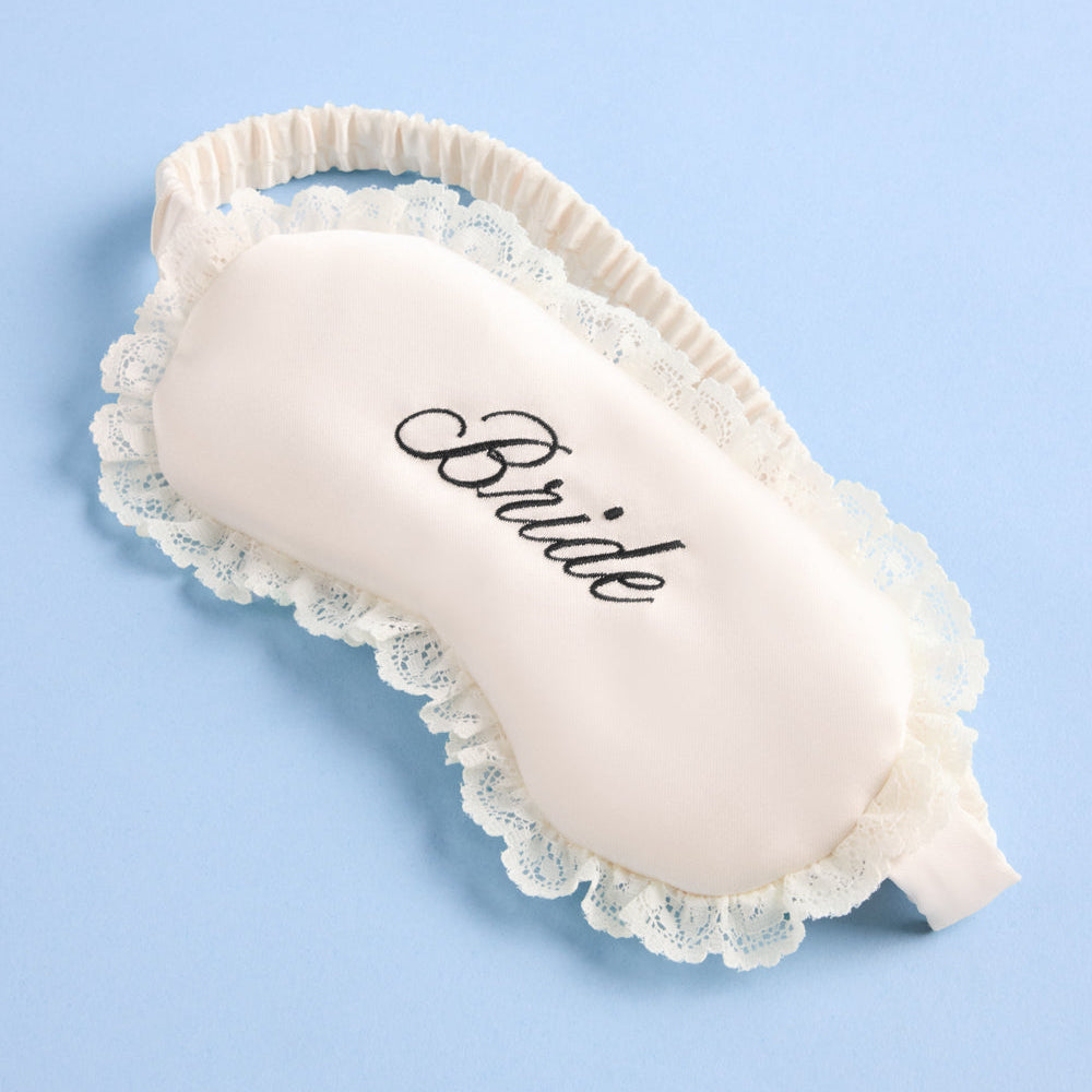 Sleep mask with lace trim and 'Bride' embroidery on a light blue background