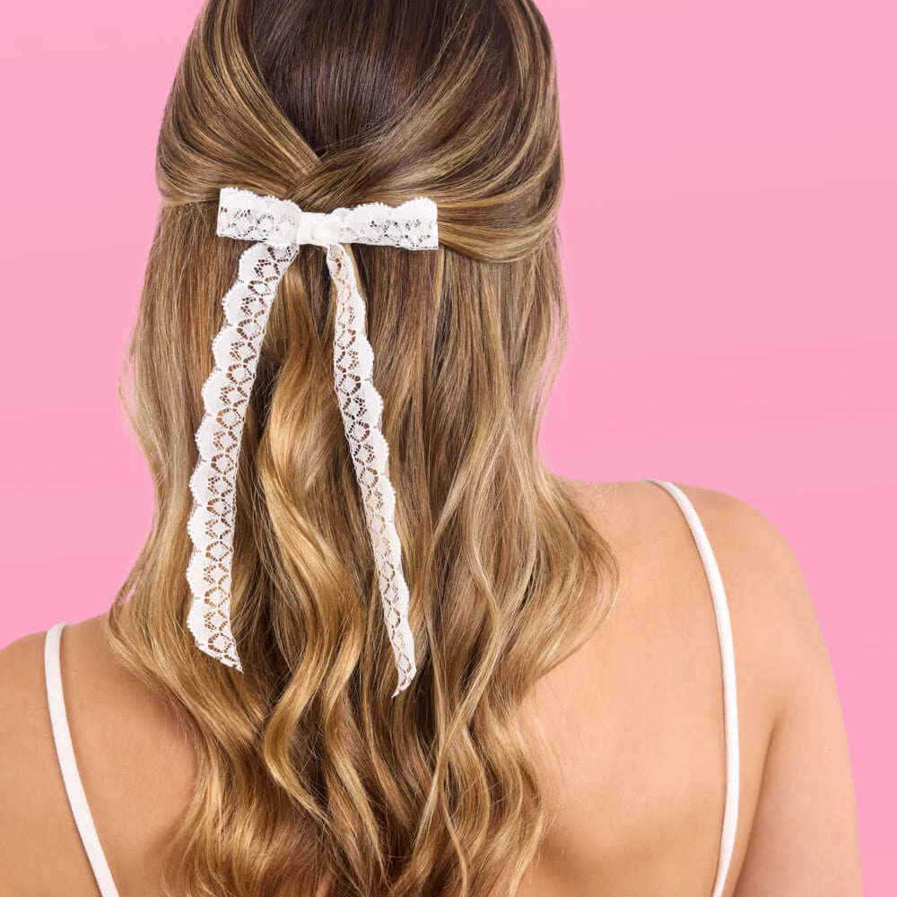 Woman with wavy hair wearing a decorative hair clip against a pink background