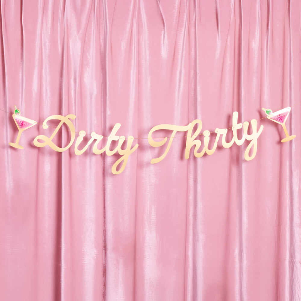 Gold 'Dirty Thirty' banner with cocktail glasses on a pink curtain background