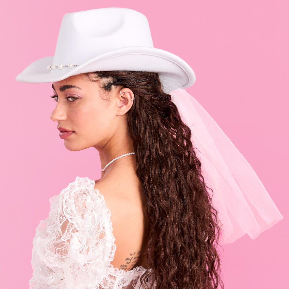 Woman wearing a white cowboy hat and lace top against a pink background