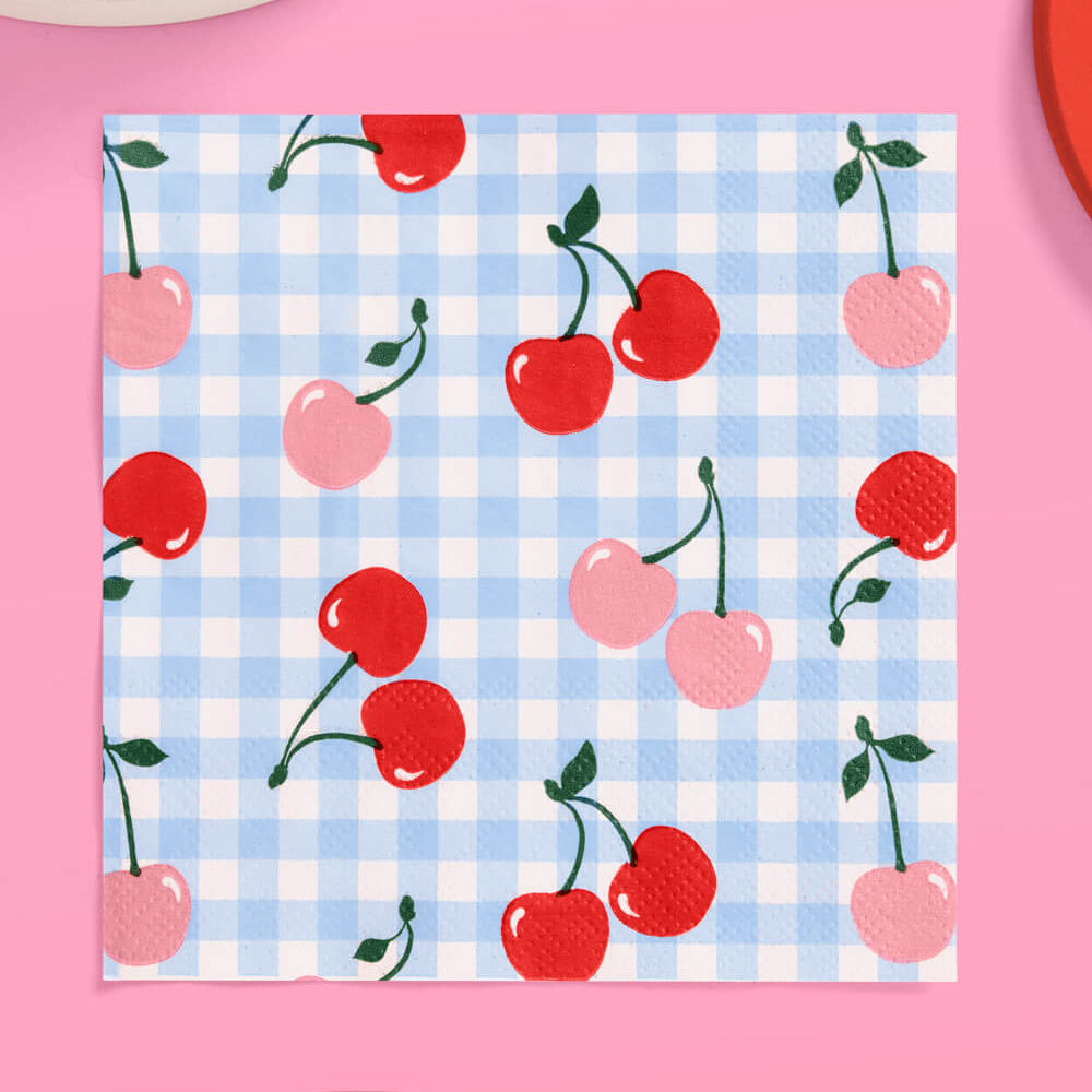 Napkin with cherry pattern on a blue checkered background, placed on a pink surface.