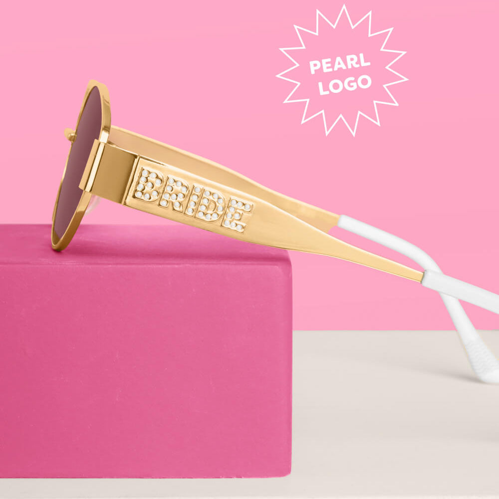 Gold sunglasses with 'Bride' on the frame against a pink background